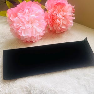 May include: A black velvet pouch with a drawstring closure. The pouch is lying on a white fluffy surface.