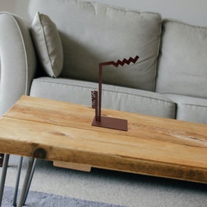 Puede incluir: Una escultura de metal marrón con un diseño en zigzag sobre una mesa de madera. La escultura es un diseño abstracto moderno.