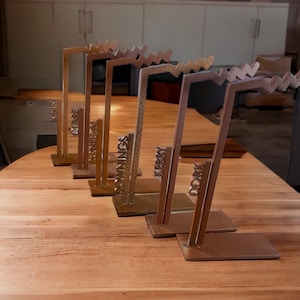 May include: Five gold-colored metal award plaques with a zig-zag design. Each plaque has a different county name on it: Kerry, Clare, Donegal, Downings, and Cork.