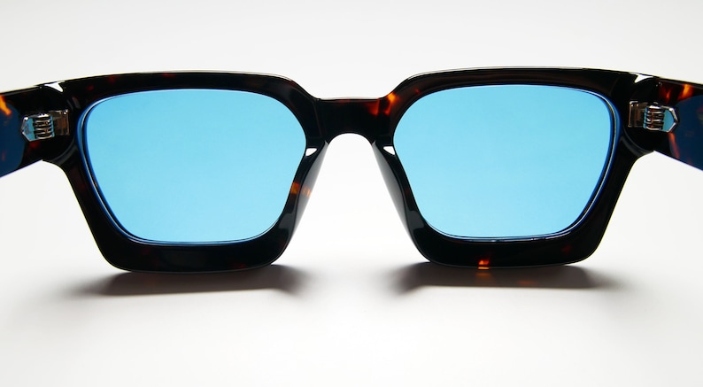 Puede incluir: Un par de gafas de sol de carey con lentes azules. Las gafas tienen una forma cuadrada y est&aacute;n hechas de pl&aacute;stico.