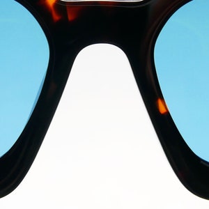 Puede incluir: Un par de gafas de sol de carey con lentes azules. Las gafas tienen una forma redondeada, de ojo de gato.