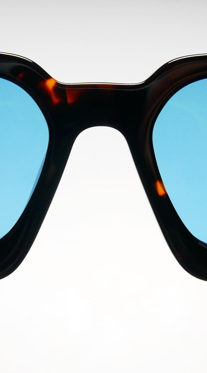 Puede incluir: Un par de gafas de sol de carey con lentes azules. Las gafas tienen una forma redondeada, de ojo de gato.