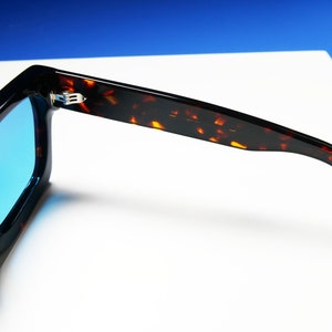 Puede incluir: Gafas de sol de carey con lentes azules. Las gafas est&aacute;n dobladas por la mitad, con las patillas de las gafas extendi&eacute;ndose hacia los lados.