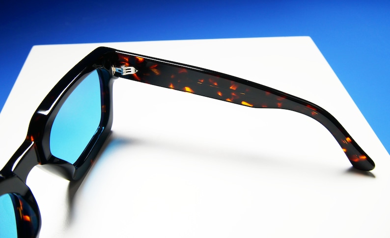 Puede incluir: Gafas de sol de carey con lentes azules. Las gafas est&aacute;n dobladas por la mitad, con las patillas de las gafas extendi&eacute;ndose hacia los lados.