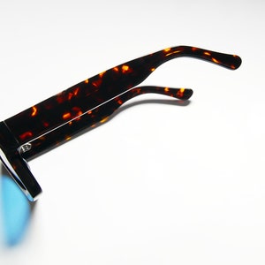 Puede incluir: Gafas de sol de carey con lentes azules espejados. Las gafas est&aacute;n dobladas por la mitad y las patillas est&aacute;n dobladas hacia arriba.