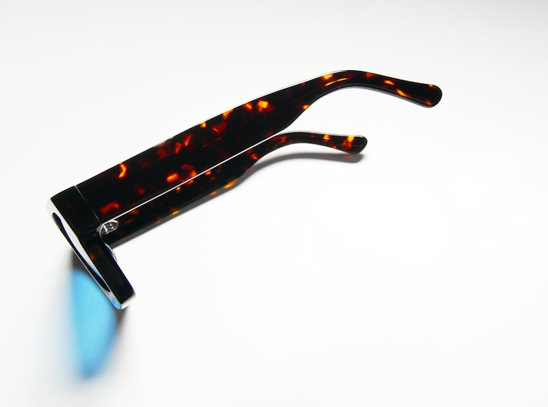 Puede incluir: Gafas de sol de carey con lentes azules espejados. Las gafas est&aacute;n dobladas por la mitad y las patillas est&aacute;n dobladas hacia arriba.