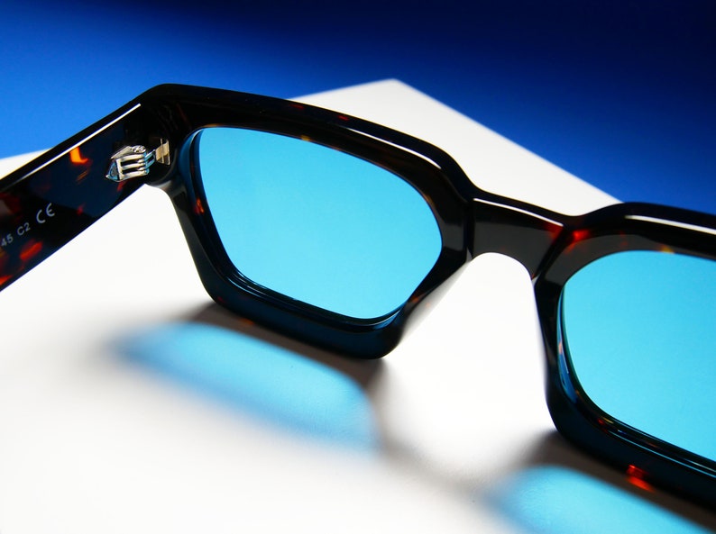 Puede incluir: Gafas de sol de carey con lentes azules. Las gafas est&aacute;n dobladas por la mitad y el interior de la montura es visible. La montura tiene el texto "45 C2 CE" en ella.