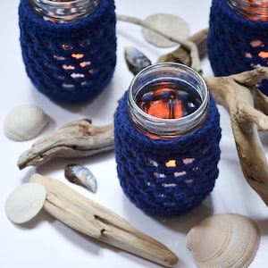 Jar lanterns decorated with navy blue jar covers and surrounded by seashells and driftwood.