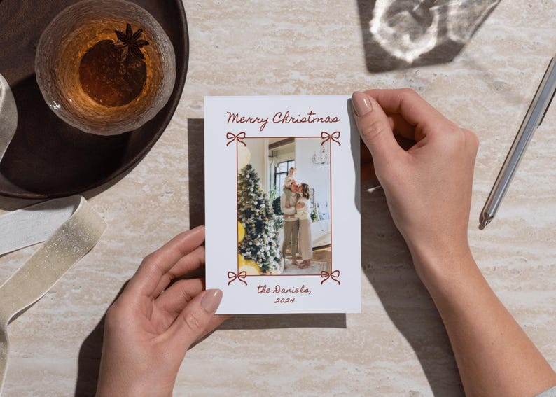 Puede incluir: Una tarjeta de Navidad blanca con un borde rojo y una foto de una familia de pie frente a un &aacute;rbol de Navidad. La tarjeta dice "Feliz Navidad" y "los Daniels, 2021".