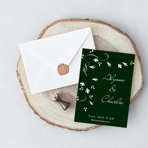 May include: A green wedding invitation with white floral designs and the text "Alyssa & Charlie" with the date and time of the wedding. The invitation is on a wooden surface with a white envelope and a wax seal.