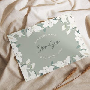 May include: Save the date card with a green background and white flowers. The text reads "Save the Date" with the names "Erin + Sam" and the date "Dec 20th, 2023".