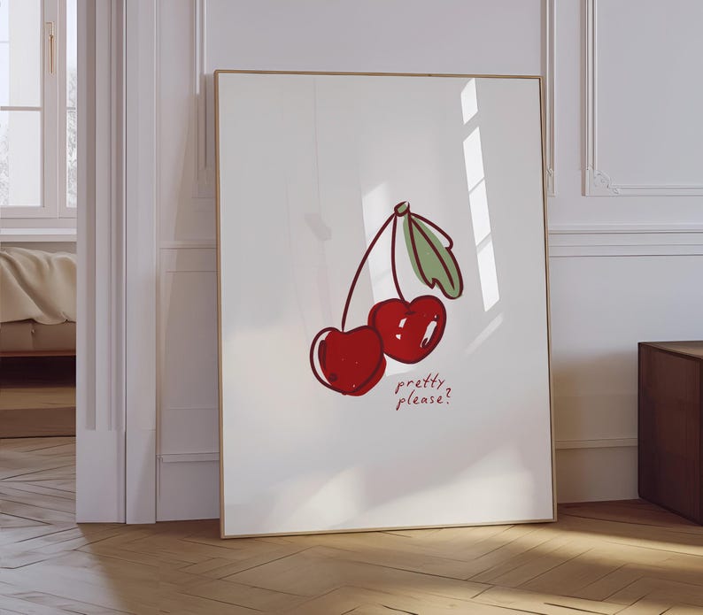Puede incluir: Una impresi&oacute;n art&iacute;stica enmarcada con una ilustraci&oacute;n caprichosa de dos cerezas rojas con hojas y tallos verdes. El texto "pretty please?" est&aacute; escrito debajo. La obra de arte se exhibe en una habitaci&oacute;n luminosa con suelo de madera.