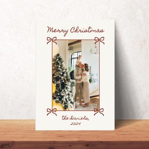 Puede incluir: Una tarjeta de Navidad con una foto de una familia de pie frente a un &aacute;rbol de Navidad decorado. La tarjeta tiene un dise&ntilde;o de lazo rojo y el texto "Feliz Navidad, los Danielo, 2024".