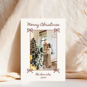 Puede incluir: Una tarjeta de Navidad con una foto de una familia de pie frente a un &aacute;rbol de Navidad decorado. La tarjeta es blanca con un borde rojo y el texto "Merry Christmas" y "the Daniels, 2024" en rojo.