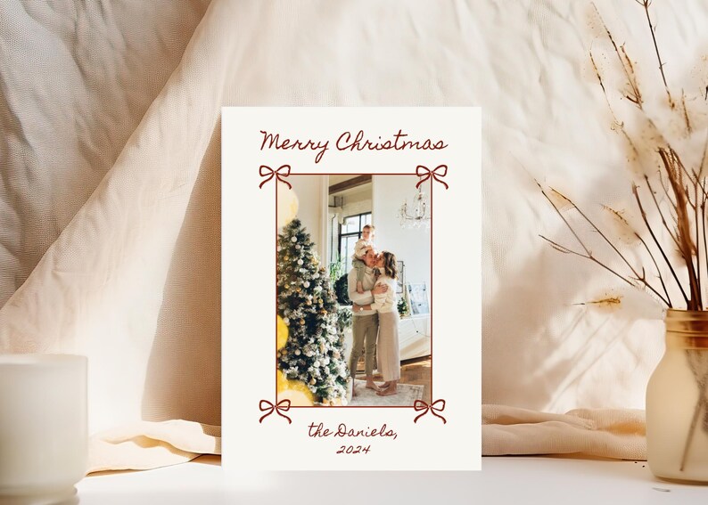 Puede incluir: Una tarjeta de Navidad con una foto de una familia de pie frente a un &aacute;rbol de Navidad decorado. La tarjeta es blanca con un borde rojo y el texto "Merry Christmas" y "the Daniels, 2024" en rojo.