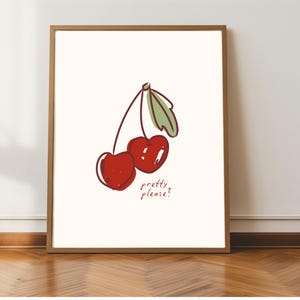 Puede incluir: Una impresi&oacute;n art&iacute;stica enmarcada con una ilustraci&oacute;n caprichosa de dos cerezas rojas con hojas verdes. La frase "pretty please?" est&aacute; escrita debajo de las cerezas en un estilo manuscrito. La obra de arte est&aacute; sobre un fondo crema.