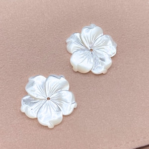May include: Two white mother of pearl flower shaped embellishments with a hole in the center.