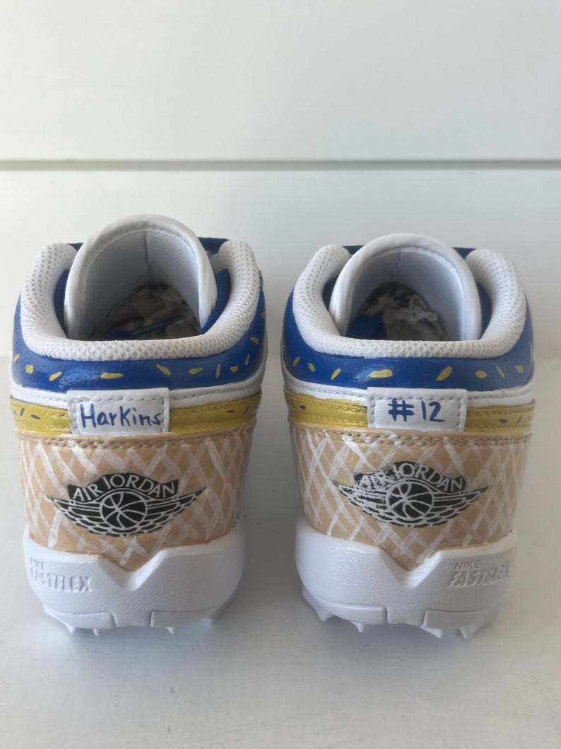Puede incluir: Par de zapatillas Air Jordan personalizadas. Los zapatos presentan una combinaci&oacute;n de colores azul, amarillo y beige con el logotipo de Air Jordan. La palabra "Harkins" est&aacute; escrita en un zapato y "#12" en el otro. Las suelas son blancas.