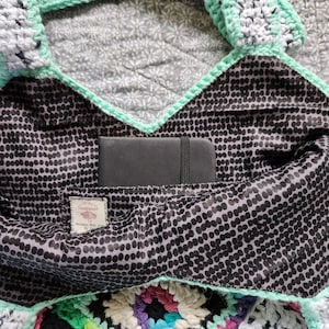 May include: A black and white polka dot fabric bag with a green crocheted trim. The bag has a pocket inside that is lined with black fabric and a small black notebook is inside the pocket.