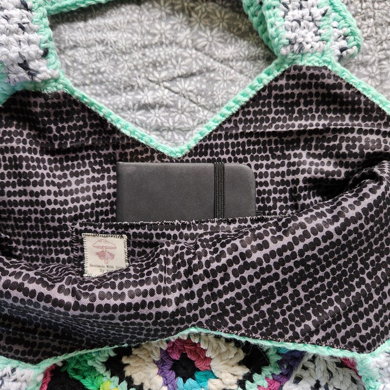 May include: A black and white polka dot fabric bag with a green crocheted trim. The bag has a pocket inside that is lined with black fabric and a small black notebook is inside the pocket.