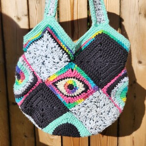 May include: A crocheted tote bag with a patchwork design featuring colorful eye motifs and black, white, and green squares.