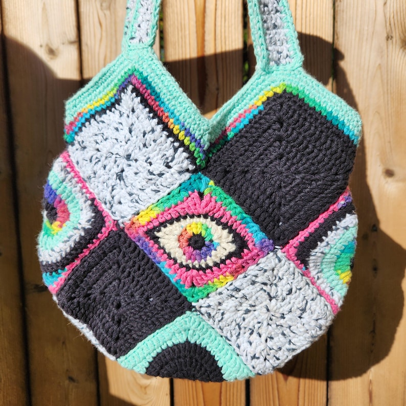 May include: A crocheted tote bag with a patchwork design featuring colorful eye motifs and black, white, and green squares.