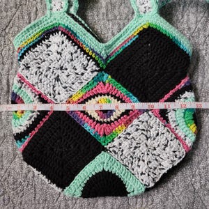 May include: A crocheted tote bag with a patchwork design featuring black, white, green, and pink squares. The bag has a unique, handmade look.