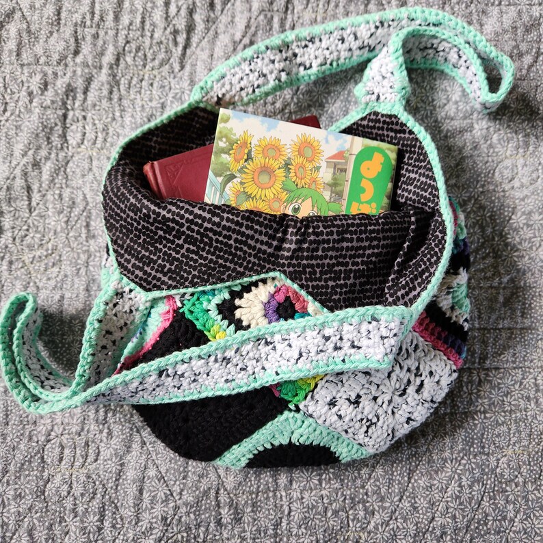 May include: A black and white crocheted tote bag with a green and white crocheted strap. The bag is filled with books, including one with a sunflower design.
