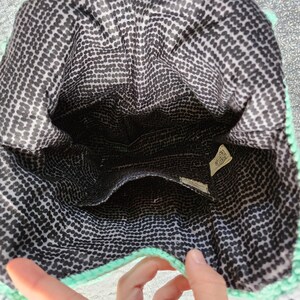 May include: The inside of a light green crocheted bag with a black and white polka dot lining. The bag has a small pocket on the inside.