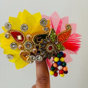 May include: A colorful, ornate headpiece with yellow, red, and green accents. The design features intricate gold-toned metalwork, sparkling rhinestones, and a cluster of multi-colored beads. The headpiece is likely for festive occasions.