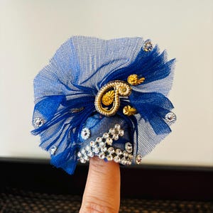 May include: A blue tulle fingertip ring with gold and silver embellishments. The ring is decorated with rhinestones and a gold paisley design.