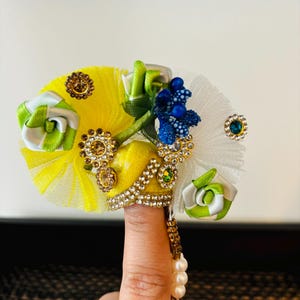 May include: A yellow and white crown with a blue and green flower, adorned with rhinestones and pearls.