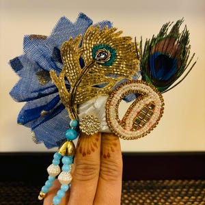 May include: A blue and gold beaded peacock feather headdress with a white and pink beaded circle and a blue and white beaded tassel.