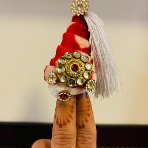 May include: A red and white cone-shaped hat with a white tassel and gold and clear rhinestone embellishments.