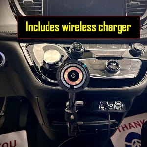 May include: A black wireless phone charger mounted in a car. The charger is attached to a black metal arm and is positioned near the car's radio controls. The text "Includes wireless charger" is visible in the image.