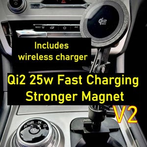 Op de afbeelding: Een zwarte ronde magnetische draadloze oplader gemonteerd op een verstelbare arm in de middenconsole van een voertuig. Het apparaat toont de tekst "Qi2" en "Includes wireless charger", "Qi2 25w Fast Charging Stronger Magnet" en "V2" op de afbeelding.
