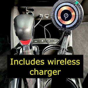 Puede incluir: Un interior de coche negro con una palanca de cambios de cuero negro, un portavasos y un cargador inalámbrico. El texto "Includes wireless charger" se muestra en la imagen.