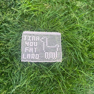 May include: A white crocheted doily with a scalloped edge. The doily is lying on a bed of green grass.