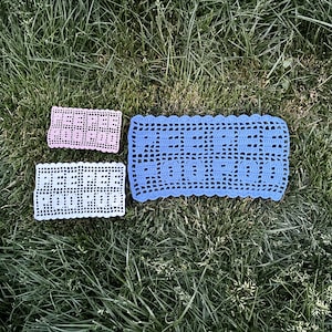 以下が含まれることがあります： 3つの異なるサイズのクロシェのドイリー。最大のドイリーは青、中くらいのドイリーは白、最小のドイリーはピンク。3つのドイリーすべてが波状の縁を持っています。