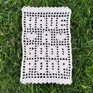 Könnte beinhalten: Eine gehäkelte Deckchen mit einem zarten Blumenmuster in hellbeige. Die Deckchen ist aus feinem Garn gefertigt und hat einen gewellten Rand.