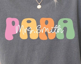 May include: A gray t-shirt with the word "PARA" in colorful, rounded letters. The text "Mrs. Smith" is written in white cursive inside the letters.