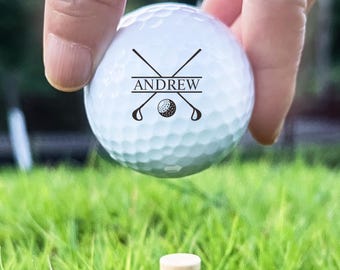 May include: A white golf ball with the name "ANDREW" printed on it, along with a golf club and ball graphic. The ball is held above a golf tee in a bed of green grass.