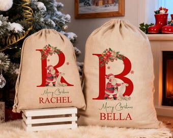 Puede incluir: Dos sacos de regalo navideños beige con letras rojas e ilustraciones de Papá Noel. Un saco dice "RACHEL" y el otro "BELLA". Ambos sacos tienen el texto "Merry Christmas".