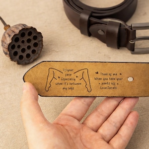 以下が含まれることがあります： シルバーのバックルが付いた茶色の革ベルト。ベルトの内側には、テキストと脚のグラフィックが刻まれています。テキストは「あなたの顔が大好きです、特に私の脚の間にあるとき。」と「ズボンを脱ぐときに私のことを考えてください - Love, Sarahi」と書かれています。