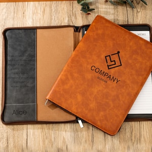 May include: A brown leather notebook with the word "COMPANY" and a logo printed on the cover. The notebook is open, revealing lined paper and a gray and tan interior. The text "A dedicated person..." is printed on the left side.