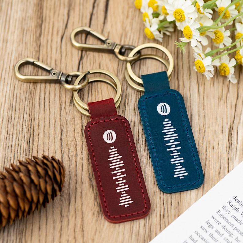 Pode incluir: Dois chaveiros de couro com argolas de metal dourado. Um chaveiro &eacute; vermelho com um design de onda sonora branca e o outro &eacute; azul com um design de onda sonora branca.