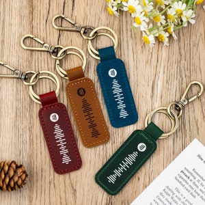 Pode incluir: Quatro chaveiros de couro de diferentes cores com um design de onda sonora branca. Os chaveiros est&atilde;o presos a argolas de metal.