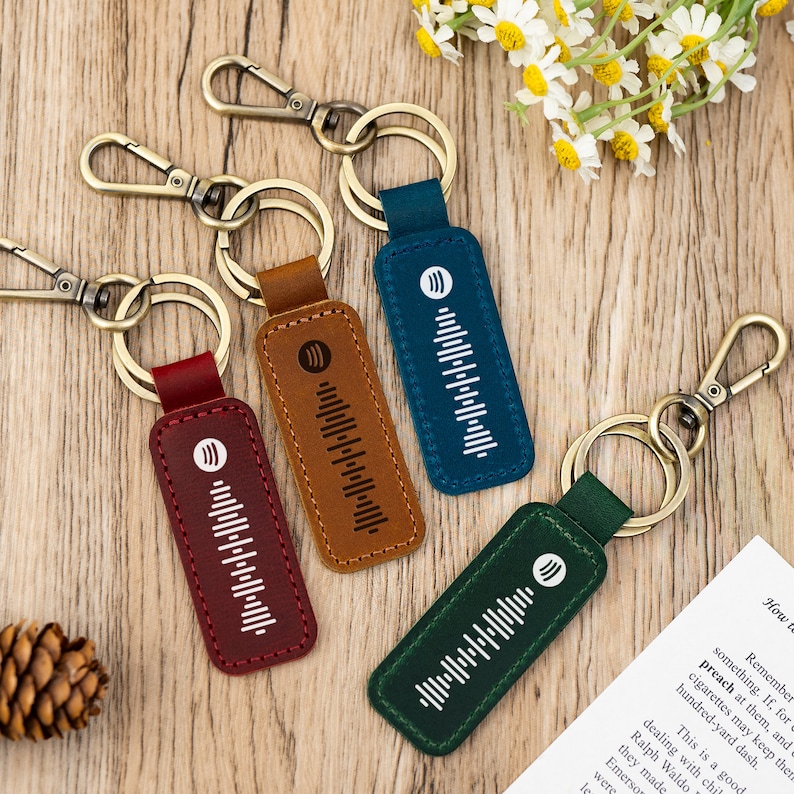 Pode incluir: Quatro chaveiros de couro de diferentes cores com um design de onda sonora branca. Os chaveiros est&atilde;o presos a argolas de metal.