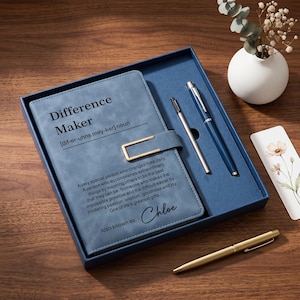 Op de afbeelding: Een blauw notitieboek met een goudkleurige metalen sluiting, voorzien van de tekst Difference Maker en een definitie, gepersonaliseerd met de naam Chloe. De set bevat twee pennen, een blauwe en een goudkleurige, in een bijpassende blauwe doos.