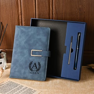 May include: A blue leather journal with a gold clasp, personalized with the initial "A" and the name "ALLEN" in black. The journal is part of a gift set that includes two pens, all presented in a blue box.